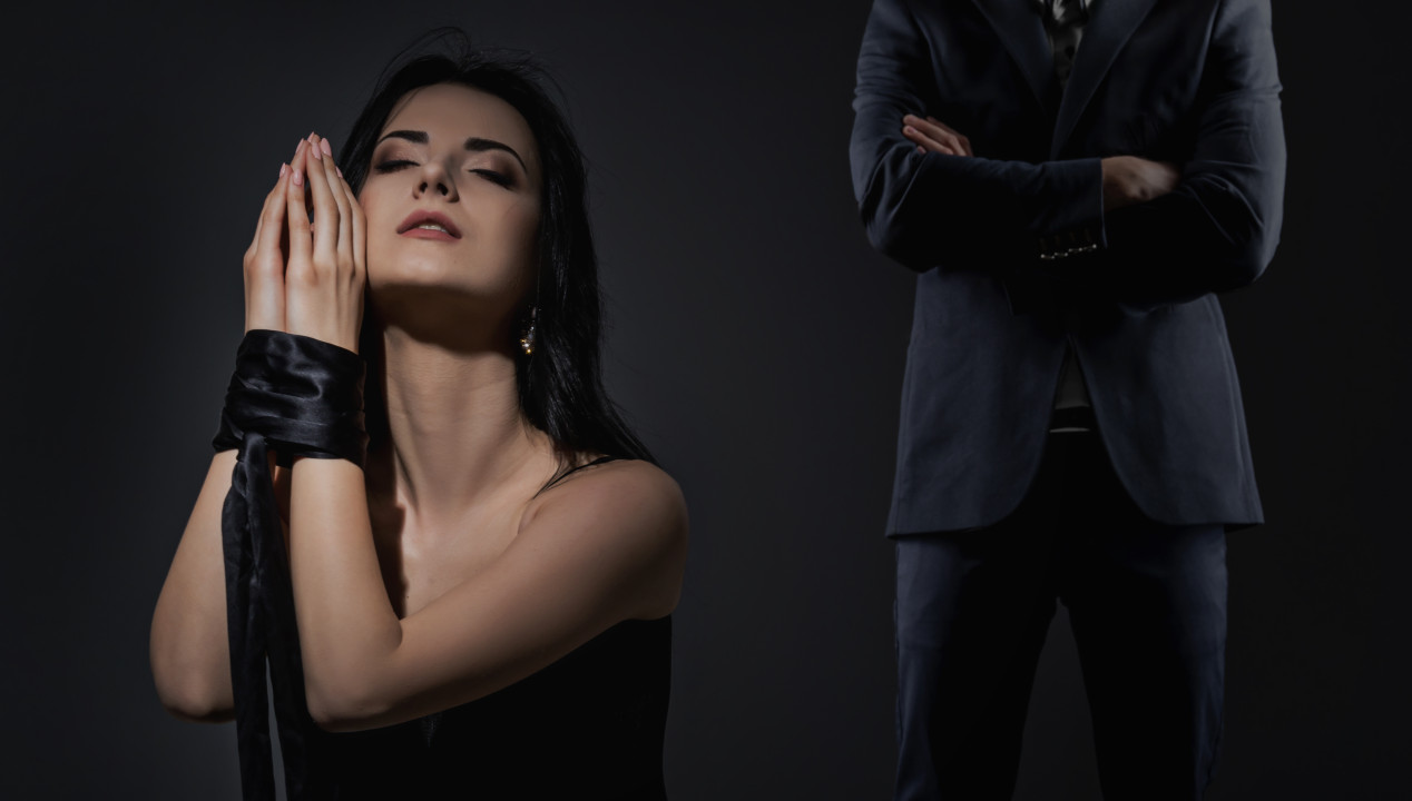 Schöne Frau mit gesselten Händen und ein Mann im Anzug vor einem schwarzen Hintergrund